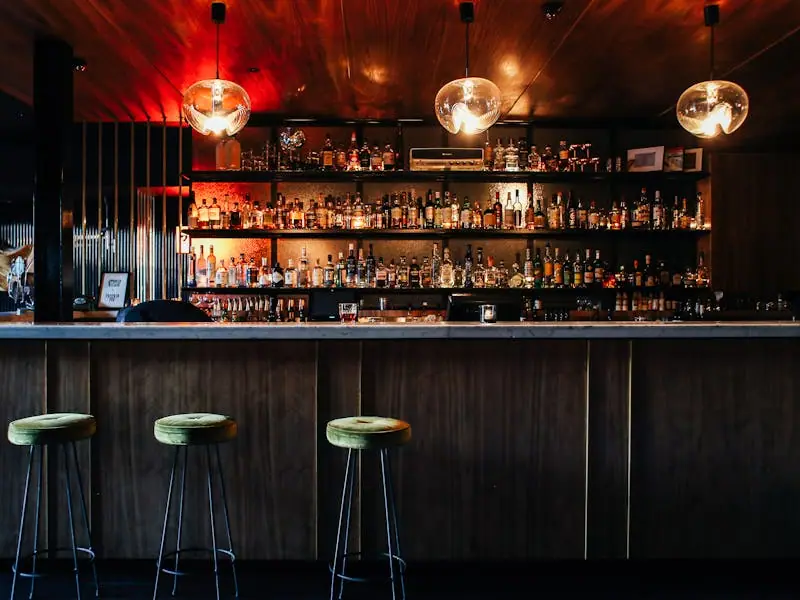 A moody back-lit cocktail bar with brass stools