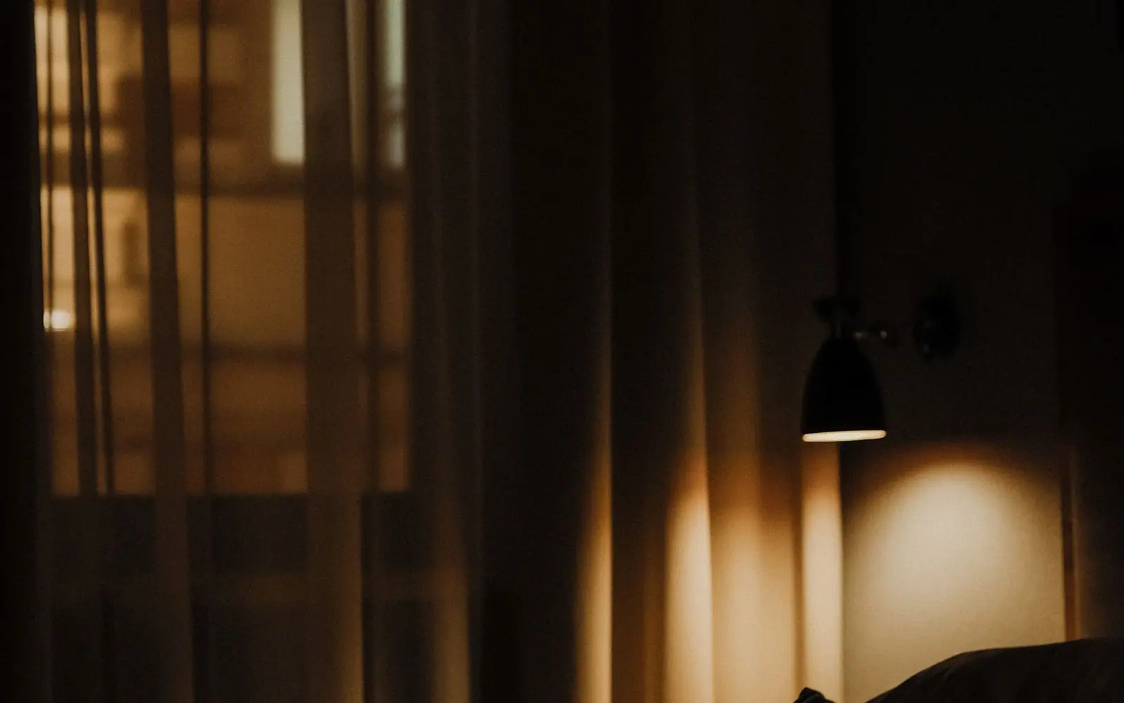 A dim, curtain-draped suite glowing with warm lamplight at dusk